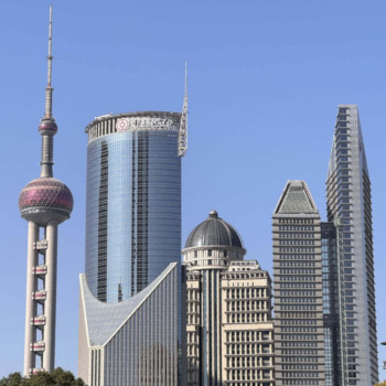 Shanghai skyline with the Oriental Pearl Tower and several modern high-rise buildings under a clear blue sky.